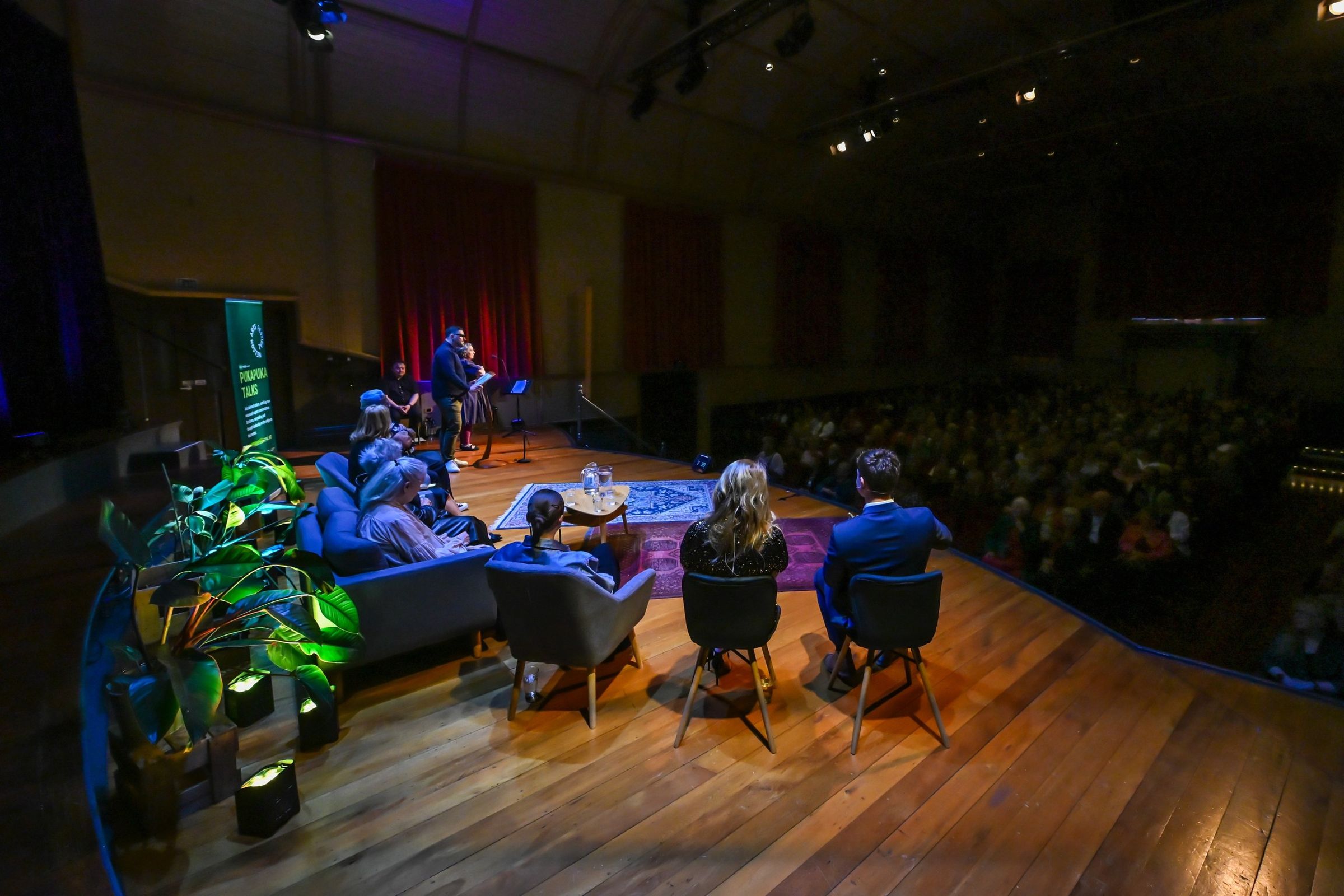 A panel on stage in a full theatre, audience in low light