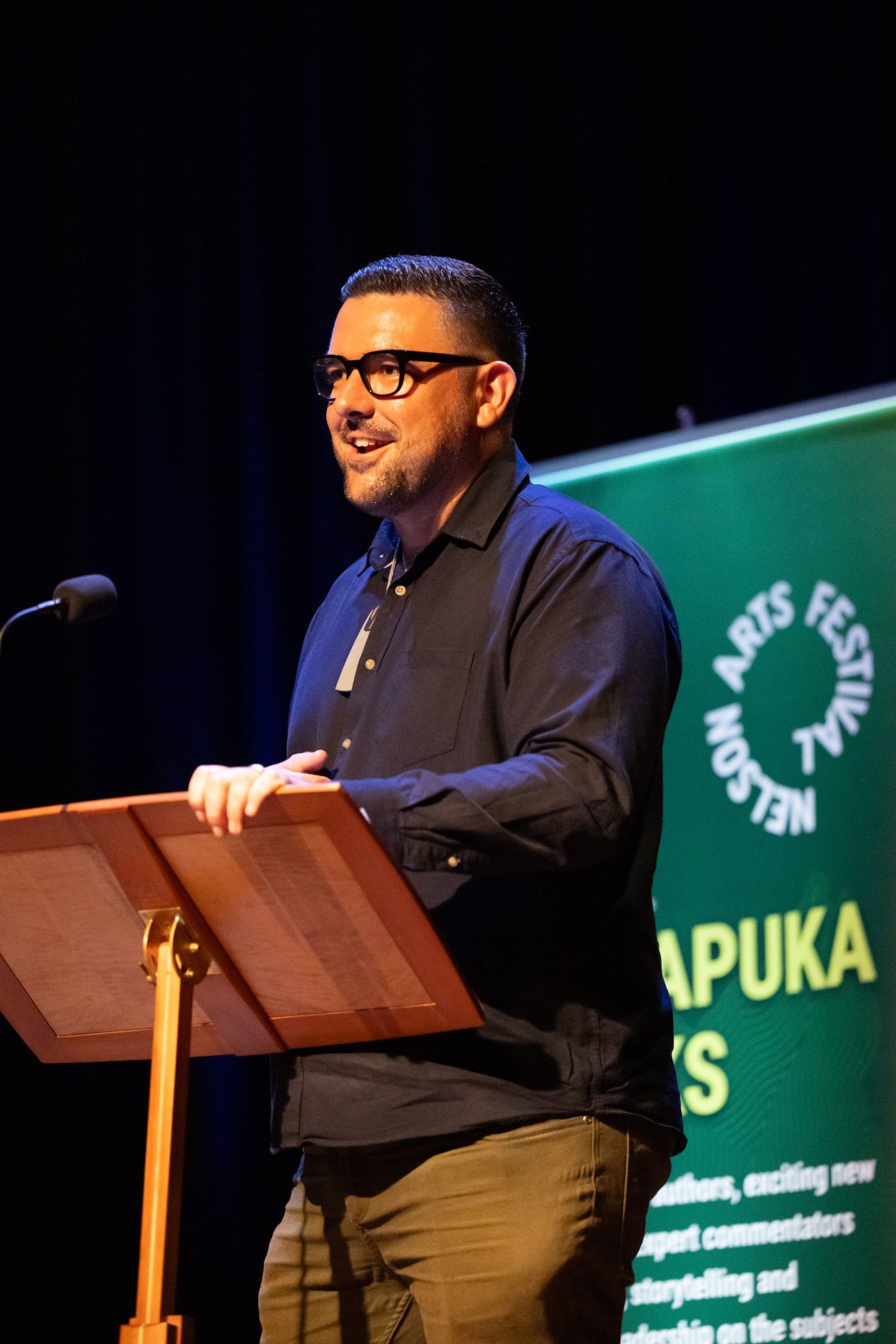 Johny O’Donnell speaking at a lectern at the Nelson Arts Festival