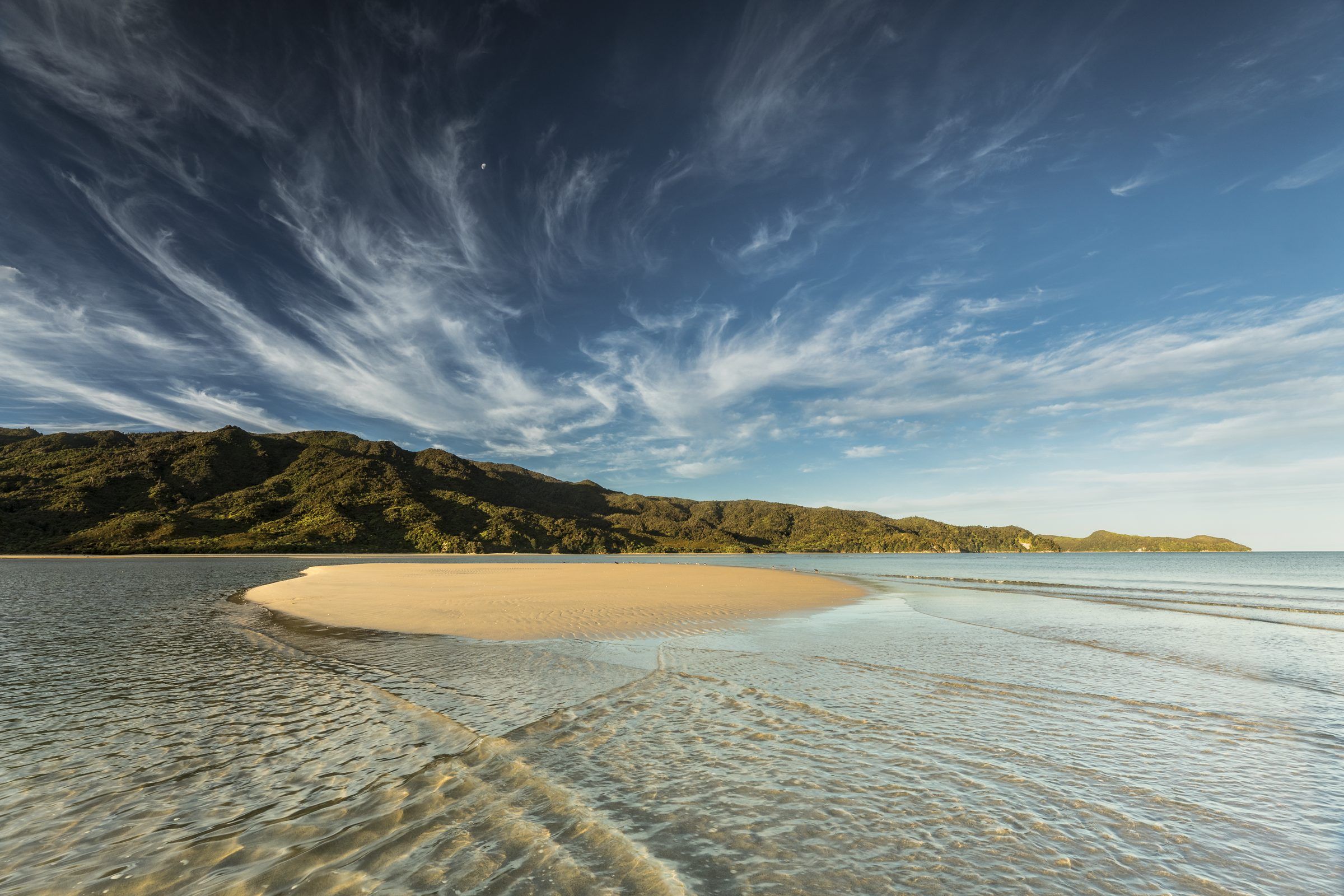 A sandbar under a wide streaked sky