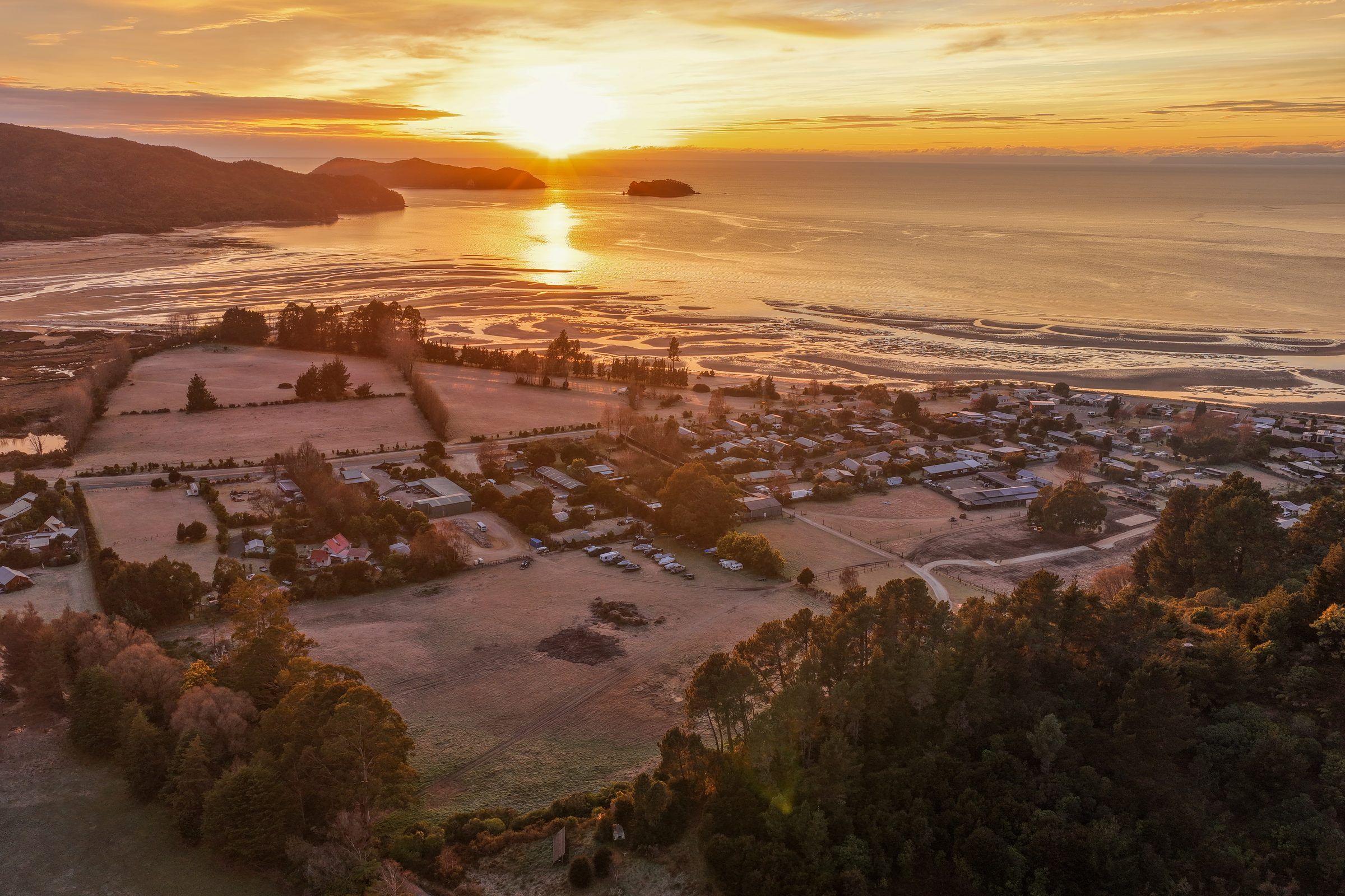 Aerial view of Mārahau and the estuary at sunset, islands on the horizon