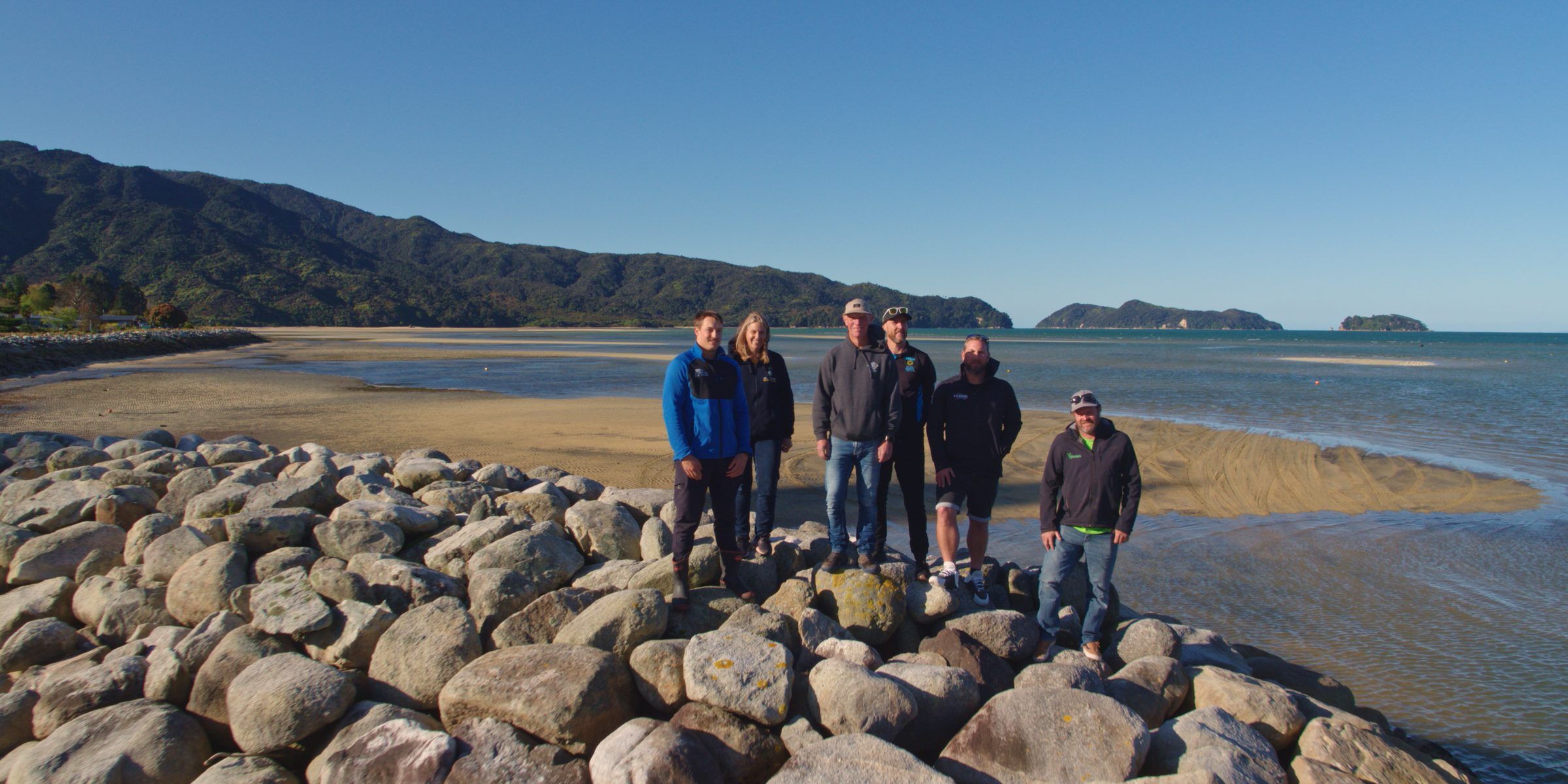 A group of local operators stand on a rock wall at the beach