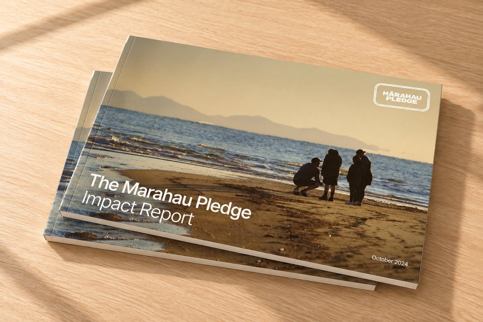 Two copies of The Mārahau Pledge Impact Report stacked on a timber table