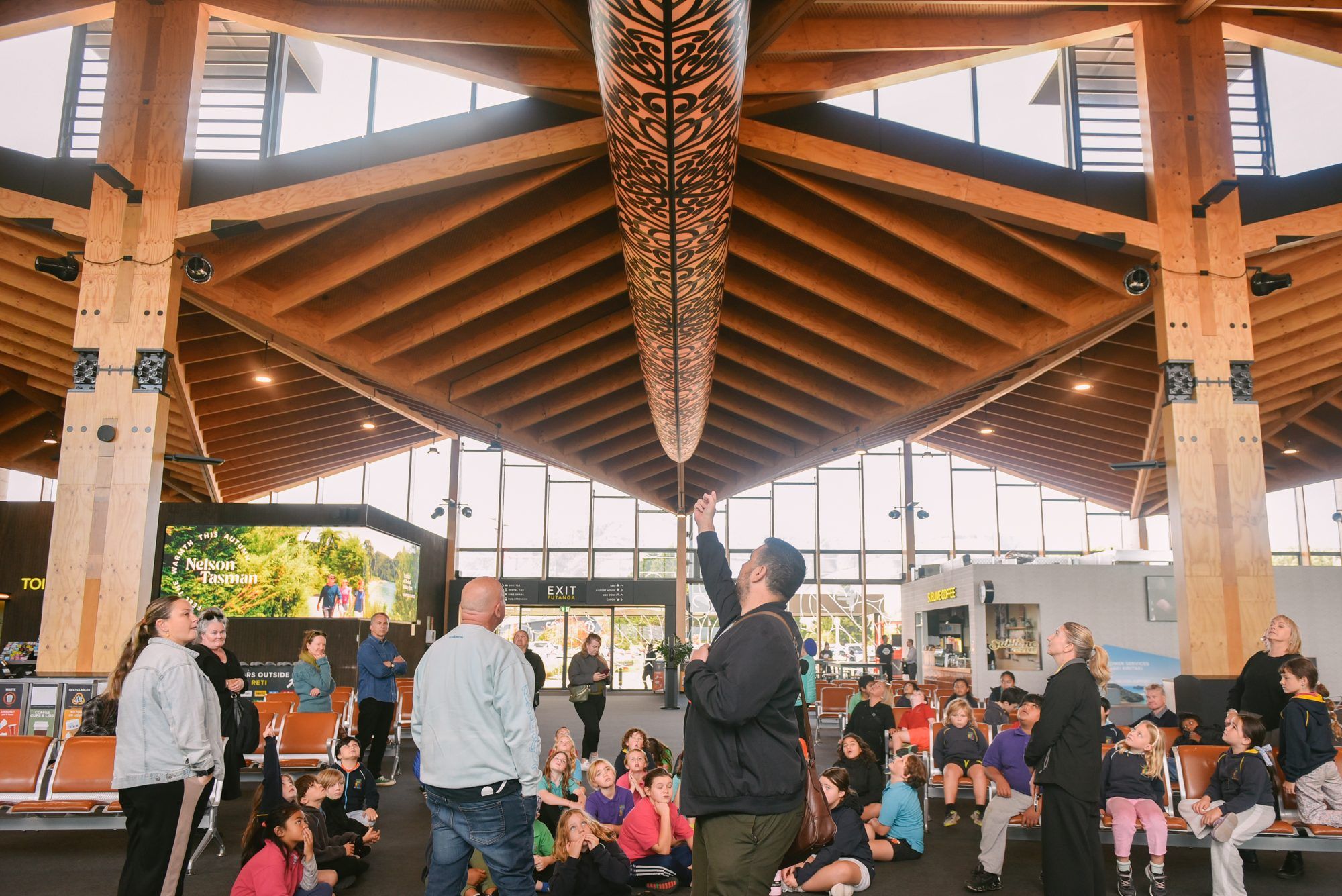 Tamariki gather beneath Aorere Ararau, the suspended waka in the Nelson Airport terminal