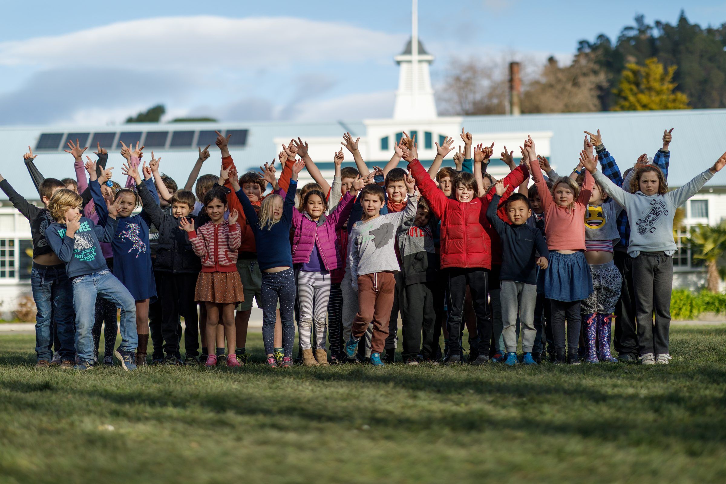 A large group of tamariki cheering with their arms raised on a school field