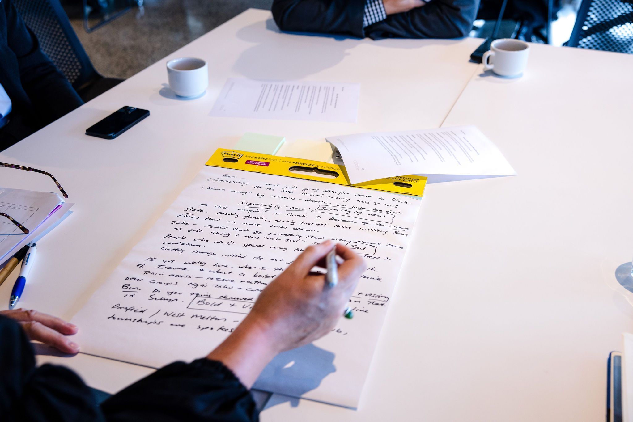 A participant writes notes on a large sheet at a table
