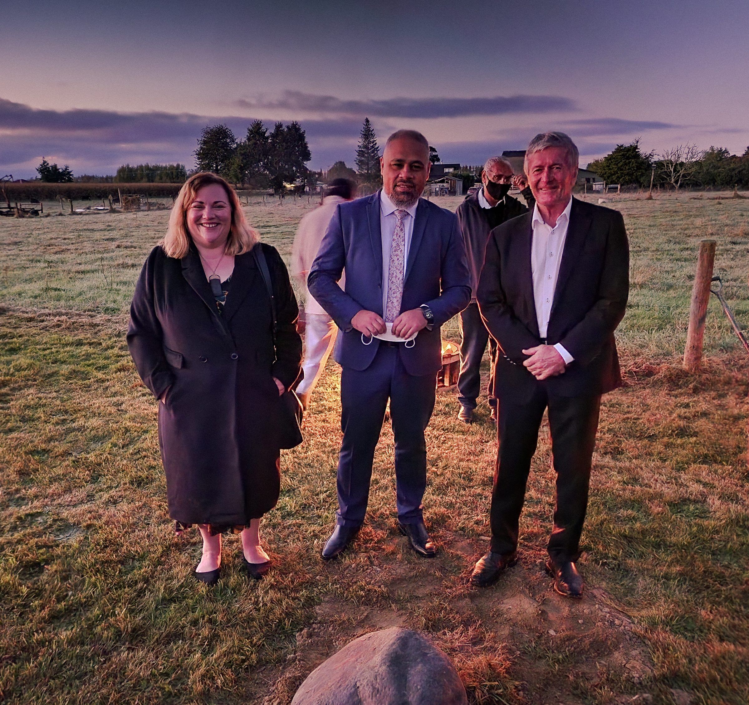 Three people stand in a paddock at dawn beside the mauri stone