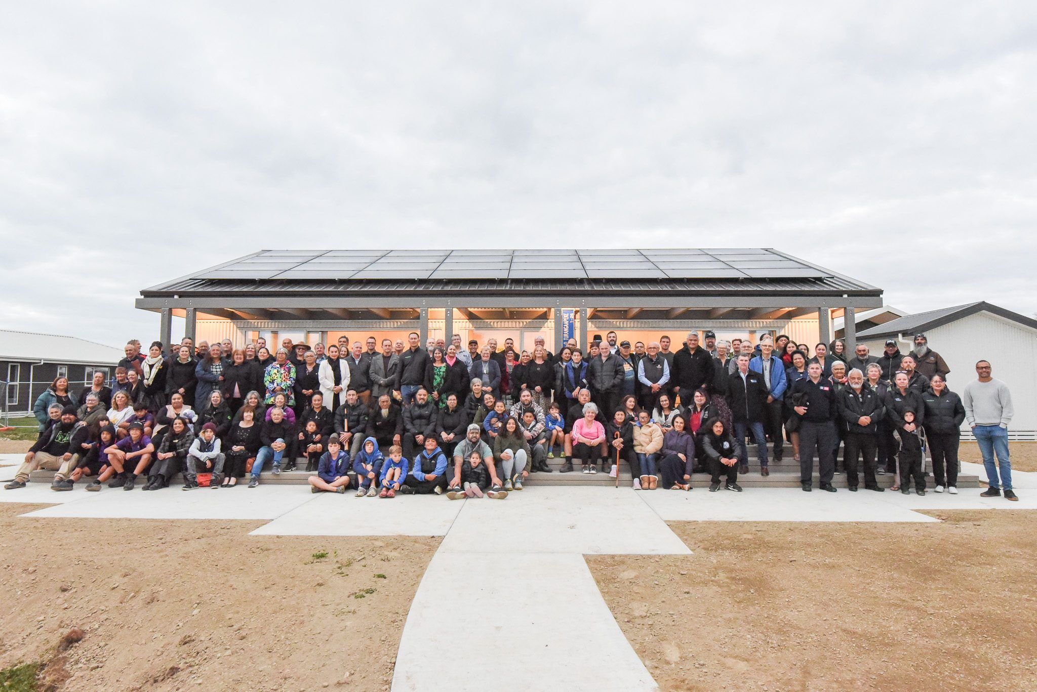 A large gathering of whānau stands together in front of the new building at Te Āwhina Marae