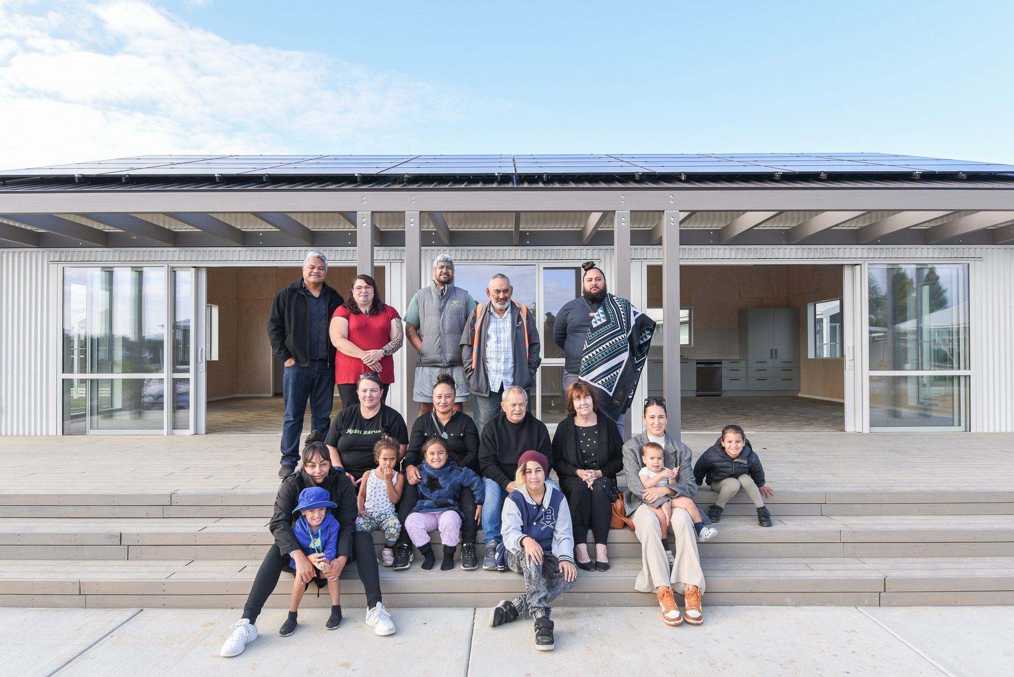 Whānau of all ages seated on the steps of the new building